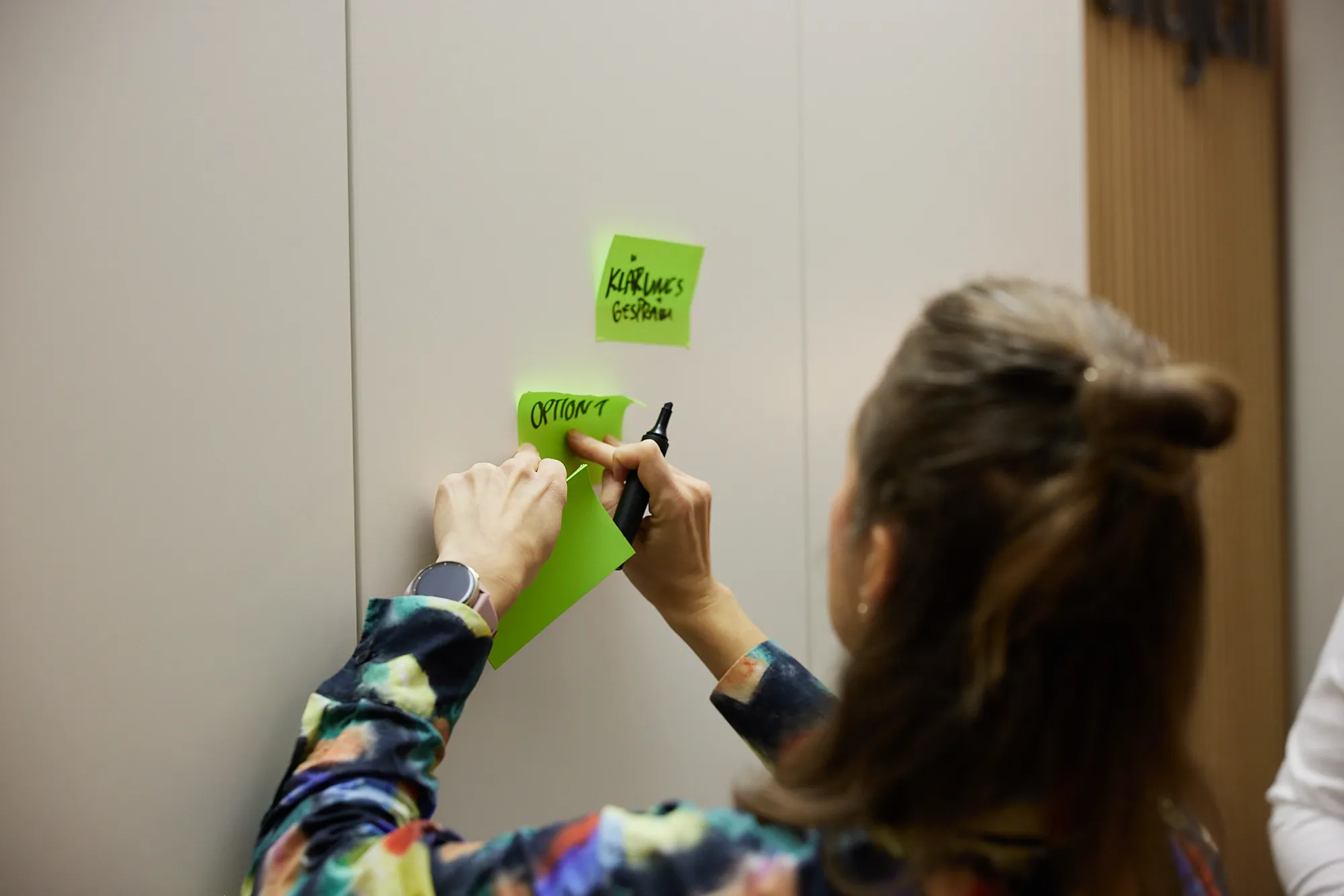 Beraterin heftet Post-It zur Leitbildentwicklung an die Wand