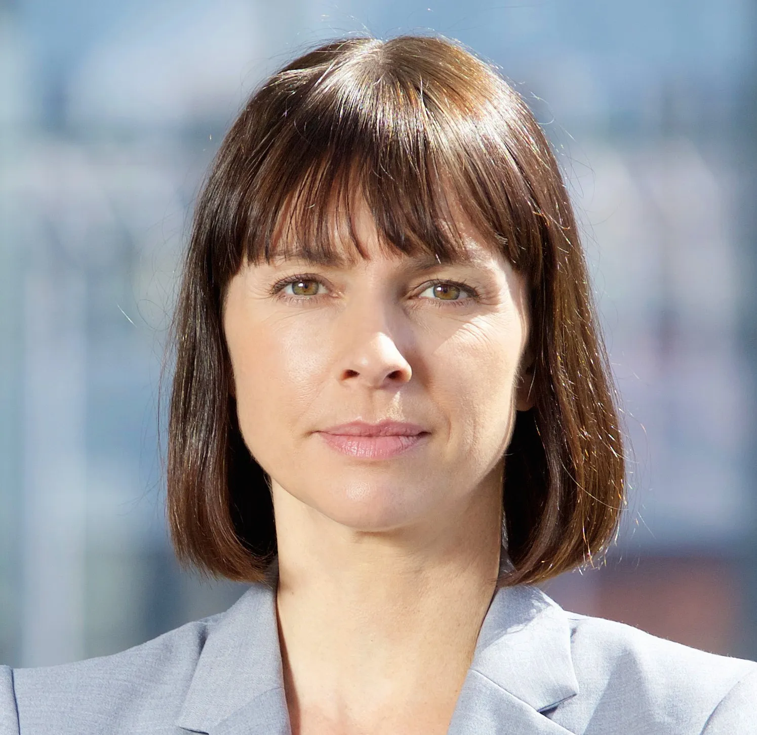 Porträt einer weiblichen Führungskraft mit braunen schulterlangen Haaren und Pony, die einen grauen Blazer trägt.